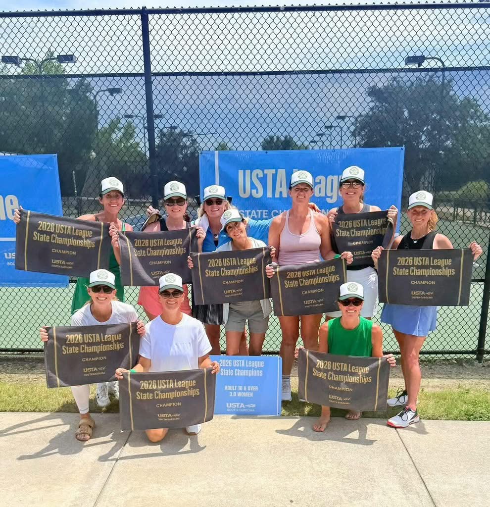 A women's tennis team poses outdoors, smiling and holding