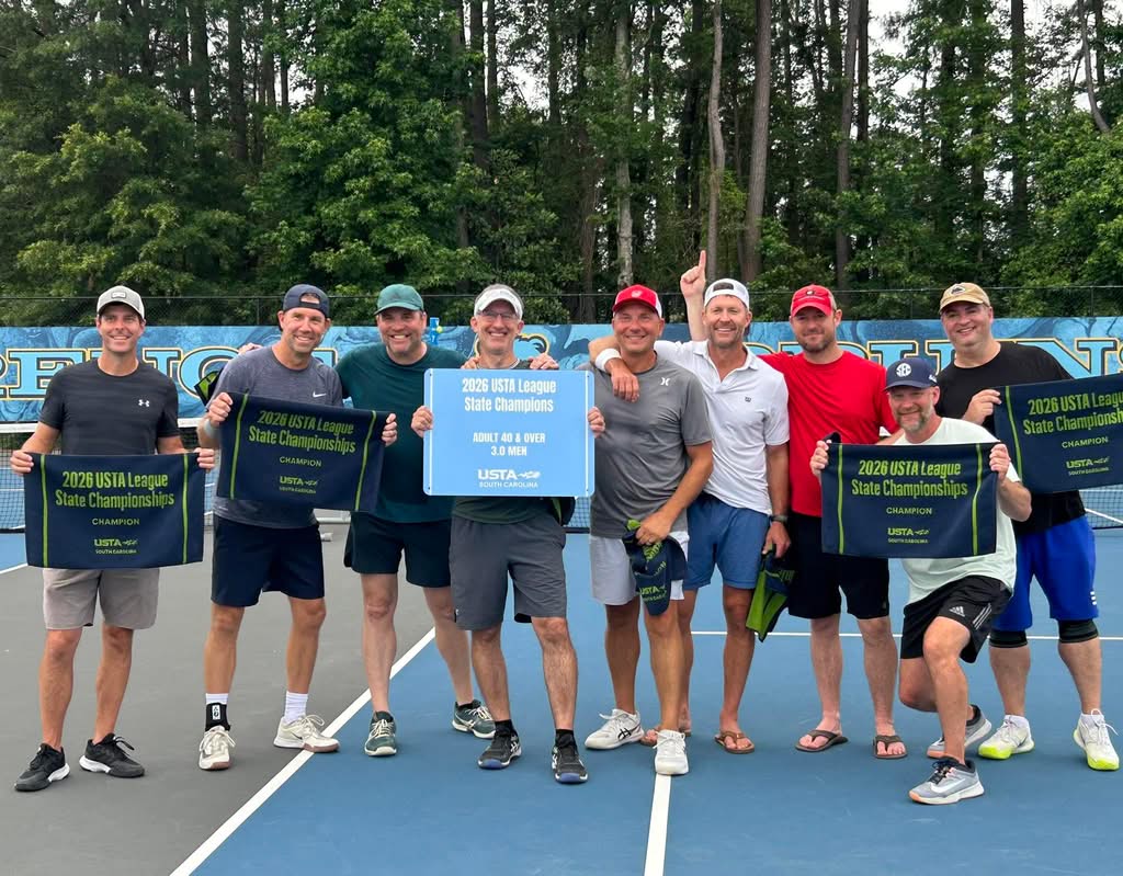 Nine men stand on a tennis court, smiling and holding blue and green banners that say