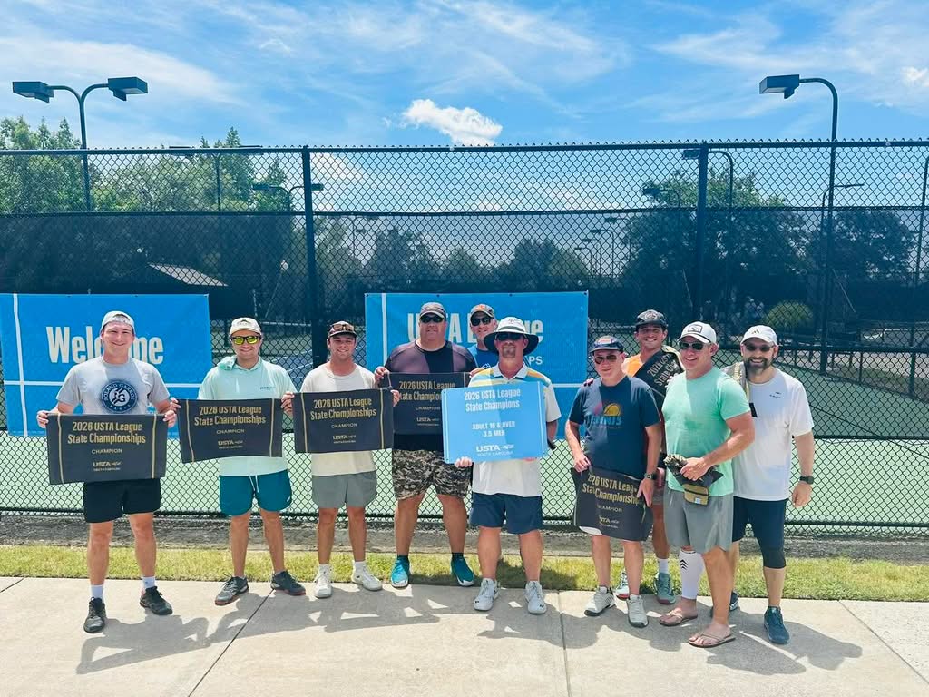 Ten men stand in front of a tennis court holding signs celebrating their 2023 USTA League State Championship win. The group smiles in bright sunlight, wearing casual athletic clothing and hats.