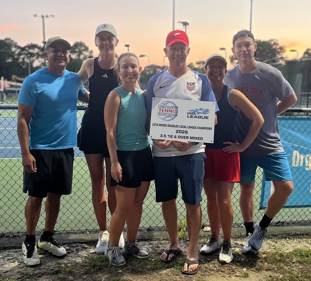 Six adults stand on a tennis court at sunset holding a sign that reads “USTA League Mixed Doubles 2024 3.5 18 & Over Mixed Champions.” They are smiling and dressed in sportswear.