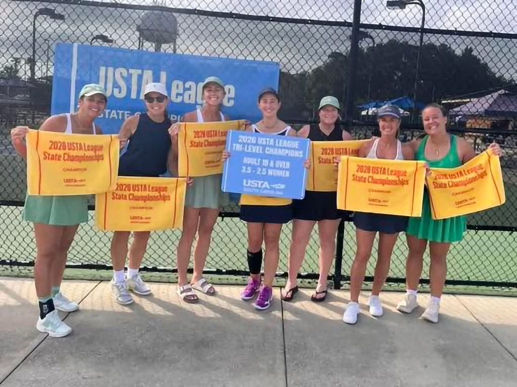 Seven women stand on a tennis court holding orange and blue banners that read “2023 USTA League State Championships” and “Tri-Level Champions.” They are smiling and posing as a team in tennis attire.
